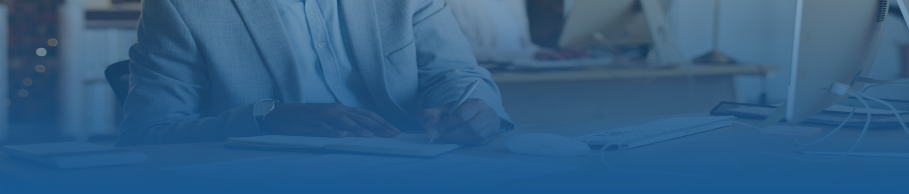 Blue tint frame of a man with a light color jacket writing on a notebook in a office space