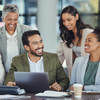 Four individuals all smiling in front of a laptop