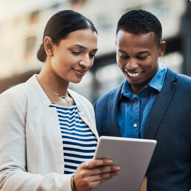 A woman with a cream jacket and a man with a blue jacket looking down at a tablet the woman is holding